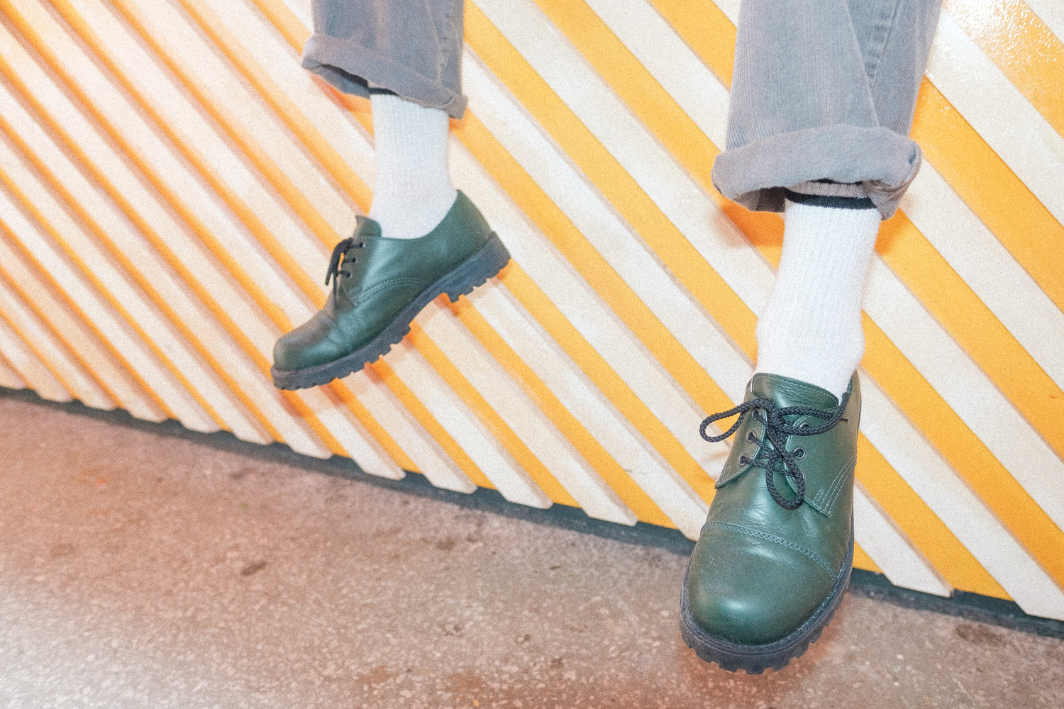 Green leather lace-up shoes with a thick black sole and paired with white socks.