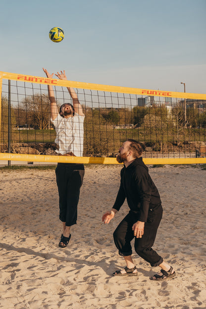 Brown leather sandals by Omaking, designed for comfort, featuring adjustable straps, worn on sandy beach during volleyball g