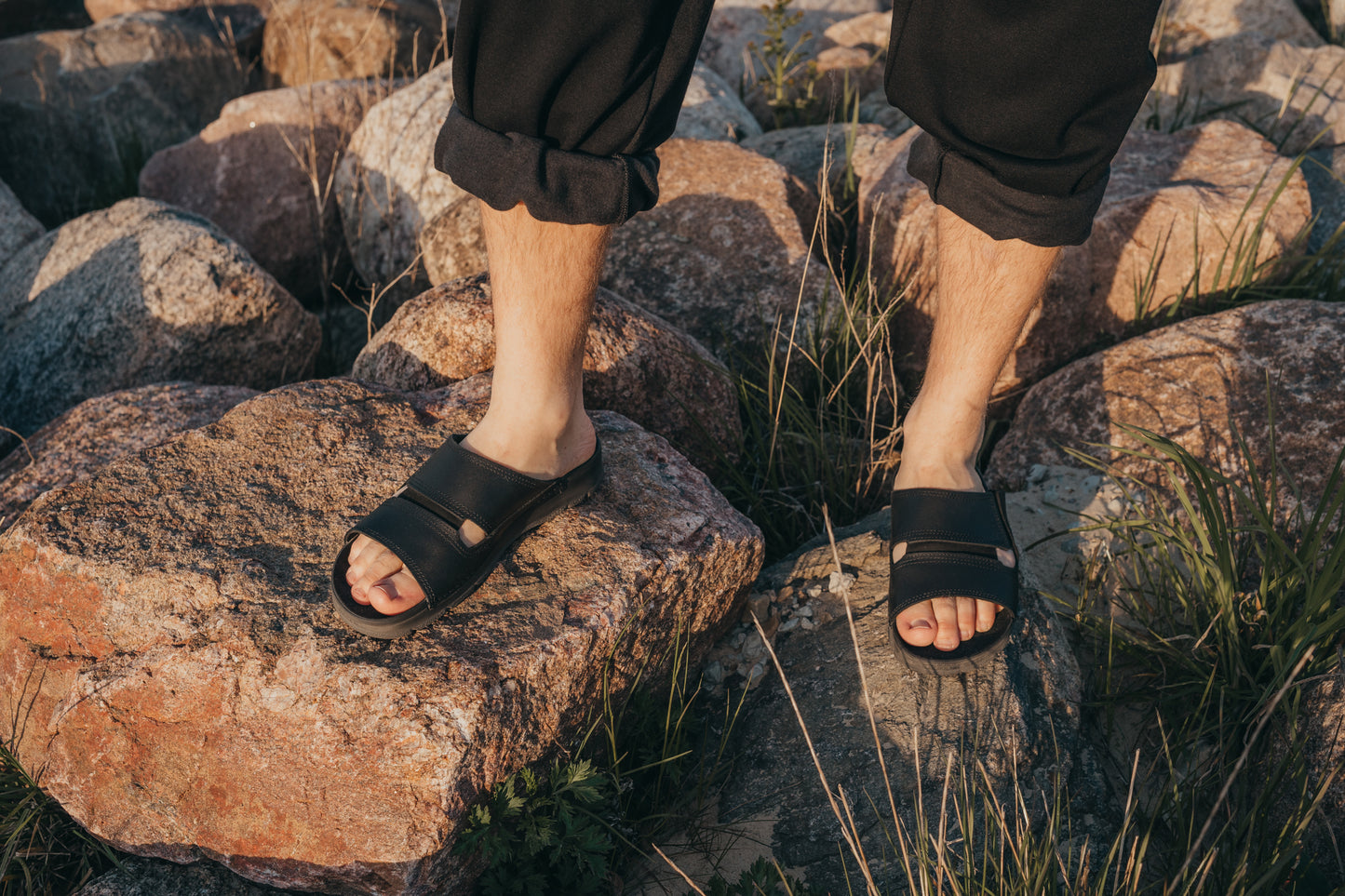 Black Miku sandals by Omaking with a sleek design, visible straps, and a comfortable fit, showcased on rocky terrain.