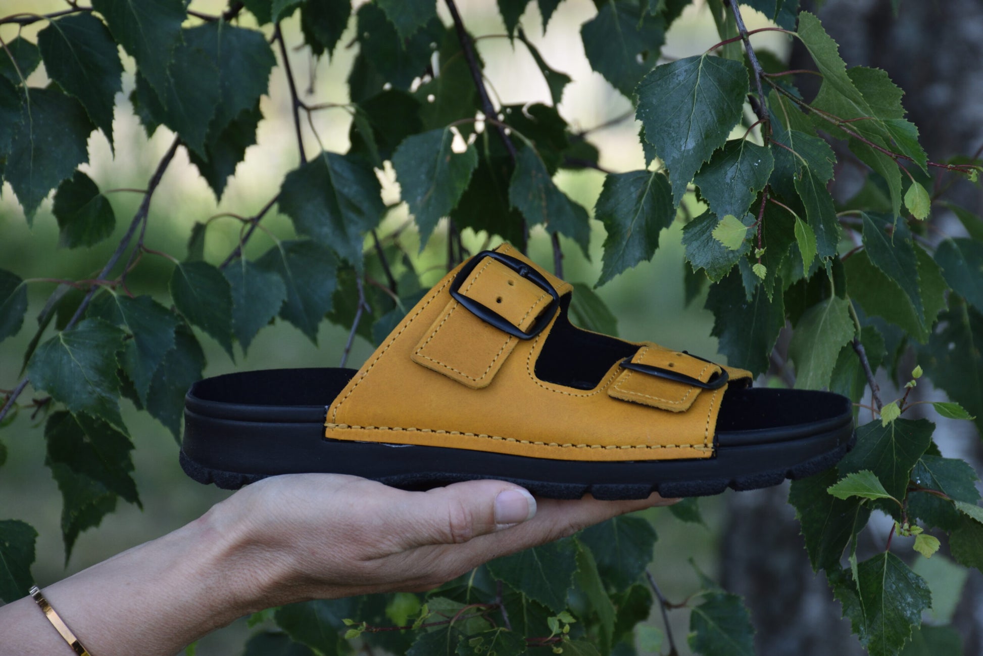 Ocre Meeliku sandals by Omaking with adjustable straps and a comfortable sole, shown against greenery.